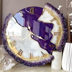 a purple and gold clock sitting on top of a table next to a white vase