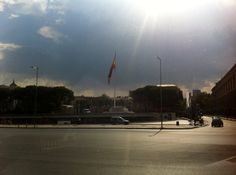 the sun shines brightly over a city street with cars driving on it and buildings in the background