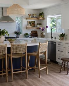 a kitchen with white cabinets and blue island in the center is surrounded by wicker chairs