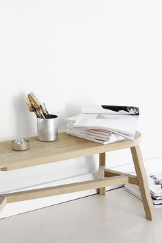 a wooden table topped with magazines and a cup filled with paintbrushes next to a white wall