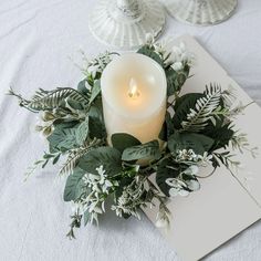 a lit candle sitting on top of a table next to some flowers and greenery