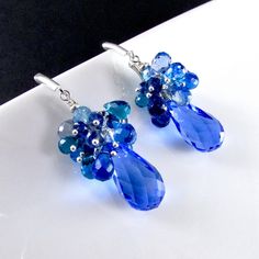 "Stunning cobalt blue lab created topaz dangle below a generous cluster of sparkling briolettes consisting of turquoise blue, navy blue, peacock green and sky blue quartz. I have used all sterling silver to keep them fresh. The gems are topped off with another blue topaz gem and a sterling silver bead. The blue topaz measure 20x11mm. The total earring length is 2 1/8\" (54mm.) from the top of the lever back ear wires." Blue Sapphire Cluster Earrings For Gift, Blue Gemstone Cluster Earrings As Gift, Blue Gemstone Cluster Earrings For Gift, Blue Faceted Drop Earrings, Blue Gemstone Accented Drop Earrings, Blue Drop Earrings With Gemstone Accents, Blue Briolette Gemstone Earrings, Blue Peacock, Earrings Handmade Dangle