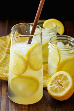 two lemons, one with a blue and white striped straw are next to a pitcher of lemonade