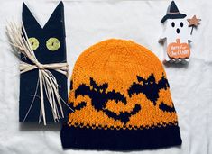 a knitted pumpkin hat next to a black cat ornament on a white sheet