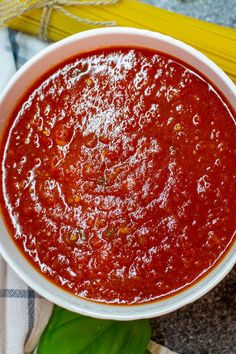 a white bowl filled with marinara sauce on top of a table next to corn