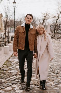 a man and woman holding hands walking down a cobblestone street in the winter