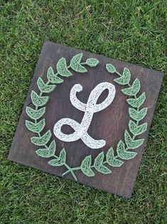 a wooden sign with the letter g painted on it in green leaves and vines is laying on grass