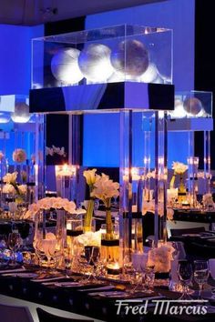 the tables are set up with clear vases and candles in front of blue lights