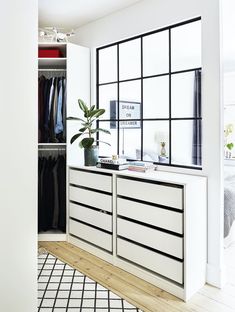 a white closet with black and white drawers next to a large window that has lots of clothes hanging on it