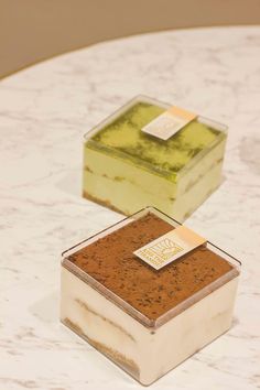 two square shaped cakes sitting on top of a white marble table next to each other