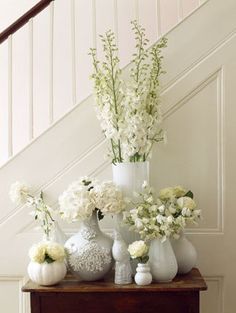 white vases and flowers are sitting on a table in front of the banister