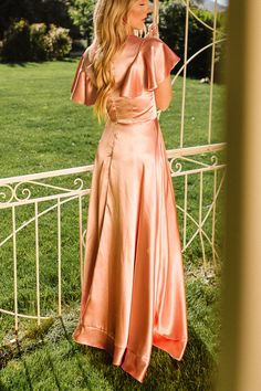 a woman in a pink dress is standing outside