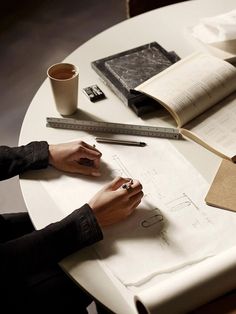 a person sitting at a table with some papers and pencils on top of it