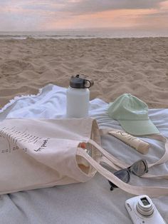 a beach towel, water bottle and sunglasses on the sand