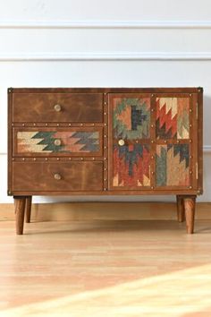 an old wooden dresser with multicolored patchwork on the doors and drawers, in front of a white wall