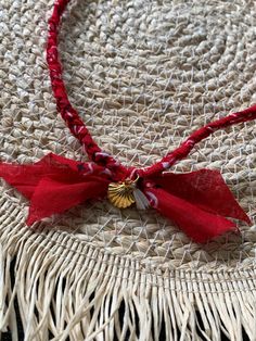 a close up of a necklace on a straw hat with red ribbon and gold charm