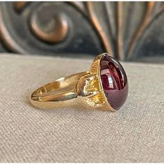 Step back to a time of refined elegance with this Victorian Garnet Signet Ring, a splendid piece that exudes the charm of the early 19th century. This impressive ring features a large cabochon garnet, measuring 14.4x11.5 mm, set in a distinctive signet style. The garnet is closed backed, emphasizing its rich, deep color and classic appeal.  Originally crafted around 1840-50, the ring has been expertly re-shanked; while the top mounting and the intricately detailed clawed feet are made of 15 karat gold, the band itself has been updated with 9 karat gold. Measuring 15.3 mm north to south and 19.3 mm across at the face, the ring sits 6 mm off the finger and narrows to 2.5 mm at the back. Weighing 4.8 grams and sized at 10, this well-loved ring showcases both historical craftsmanship and a tim Formal Domed Signet Ring With Cabochon, Classic Yellow Gold Signet Ring With Cabochon, Luxury Ruby Ring With Oval Cabochon, Antique Ruby Signet Ring, Classic Domed Cabochon Signet Ring, Classic Yellow Gold Cabochon Ruby Ring, Formal Cabochon Ruby Ring, Classic Yellow Gold Ruby Cabochon Ring, Classic Domed Cabochons With Polished Finish