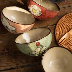 four bowls with flowers painted on them are sitting on a table next to a basket