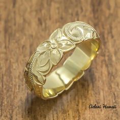 a gold ring with flowers on it sitting on a wooden table next to a coin