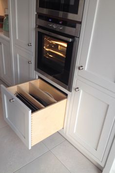 an open drawer in the middle of a kitchen with white cupboards and drawers on both sides