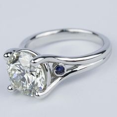 a white gold ring with an oval cut diamond and two blue sapphire stones on the side