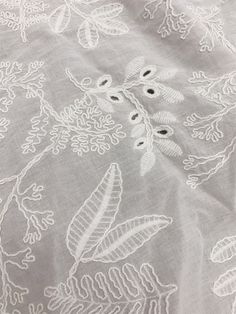 an embroidered fabric with white flowers and leaves on grey background, close - up photo