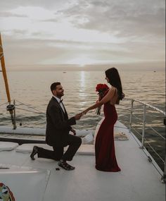 a man in a suit and tie sitting on the back of a boat next to a woman in a red dress