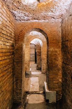 an old tunnel with brick walls and benches in the center, leading to another room