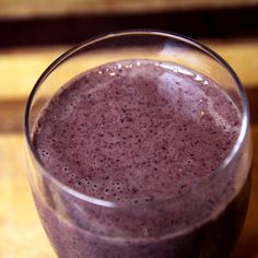 a glass filled with purple liquid sitting on top of a wooden table