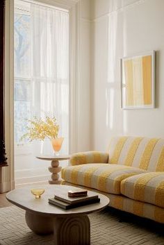 a living room with a couch, coffee table and vase on the floor in front of a window