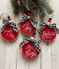 four christmas ornaments hanging on a white wooden wall with red and black plaid ribbon around them