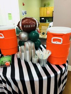 an orange and black table topped with coolers and football decorations on top of it