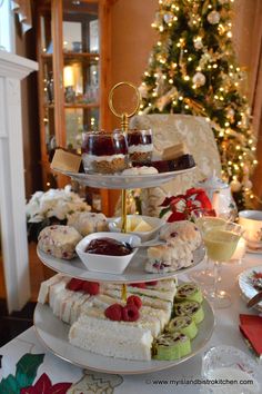 three tiered trays filled with cakes and pastries on a table in front of a christmas tree