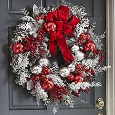 a christmas wreath with red and silver ornaments hanging on the front door to welcome guests