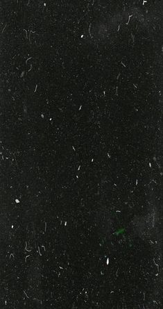 black and white photograph of snow flakes in the night sky with one green light