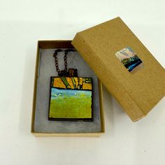 an open box with a necklace in it on top of a white table next to a brown cardboard box