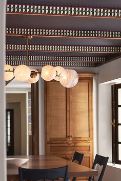 a dining room table with chairs and lights hanging from it's ceiling in front of wooden cabinets