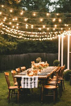 an outdoor dinner table set up with lights strung over it