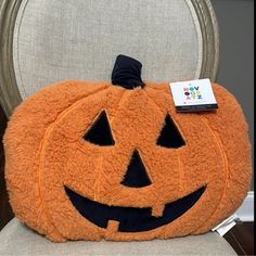 an orange pumpkin shaped pillow sitting on top of a chair with a tag attached to it