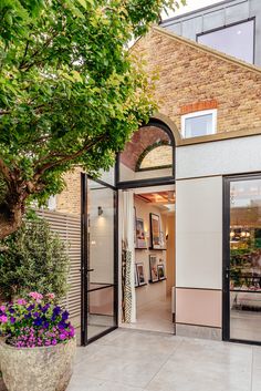 a woman walking into a building through an open door with flowers in the foreground