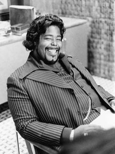 a black and white photo of a woman sitting in a chair smiling at the camera