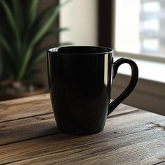 a black coffee cup sitting on top of a wooden table next to a window sill