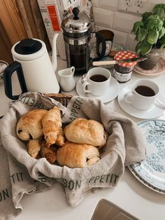 some croissants are in a basket on the kitchen counter next to coffee