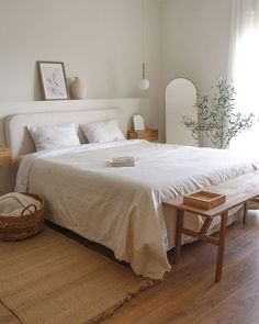 a white bed sitting in a bedroom next to a wooden table and lamp on top of a hard wood floor