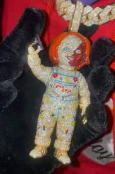 a toy doll with red hair and orange eyes is hanging from a black cord that has gold chains attached to it