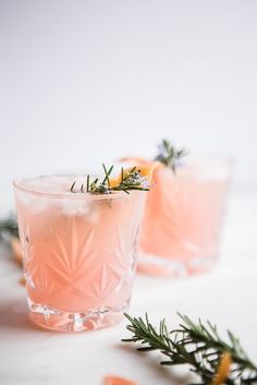 two glasses filled with pink lemonade and rosemary garnish on a white surface