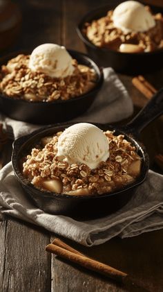 two skillets filled with apple crisp and ice cream on top of a wooden table