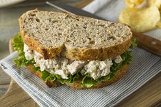 a chicken salad sandwich with lettuce on a cutting board next to potato chips