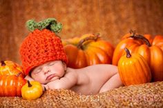 a baby wearing a knitted hat laying next to pumpkins