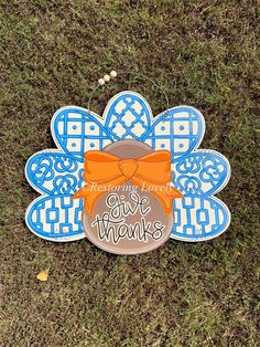 an orange bow on top of a blue and white flower shaped sign that says give thanks